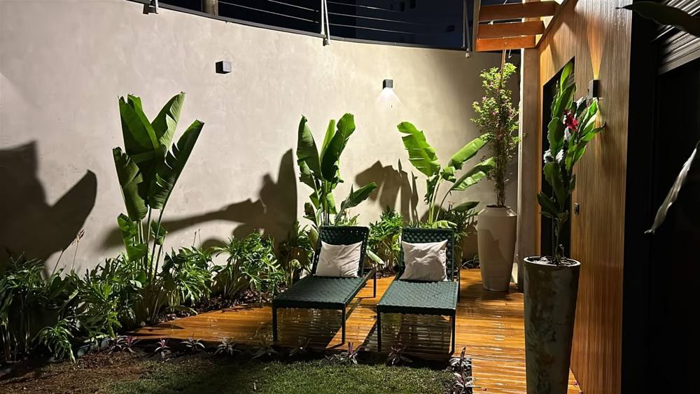 O mesmo quintal pronto à noite, com deck iluminado e bananeiras-de-jardim